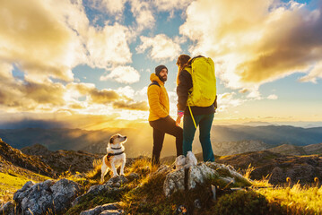 couple of mountaineers with their dog watching the sunset after hiking in the mountains. outdoor sports.