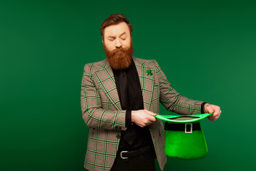 Wall Mural - Pensive bearded man looking at saint patrick day hat isolated on green.