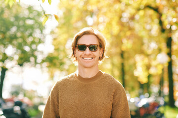 Wall Mural - Outdoor autumn portrait of handsome young man wearing brown fuzzy fleece sweater and sunglasses