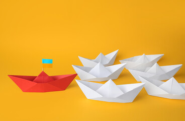 Wall Mural - Group of paper boats following red one on yellow background. Leadership concept