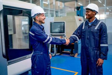 Wall Mural - Caucasian worker and African American technician shake hand with smiling face in front of factory robotic machine during work in workplace.