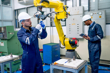 Wall Mural - Caucasian engineer or technician worker hold part of robotic arm and check  the function of machine and African American co-worker support in the back in factory workplace.