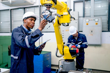 Wall Mural - African American engineer or technician worker hold part of robotic arm and check  the function of machine and co-worker support in the back in factory workplace.