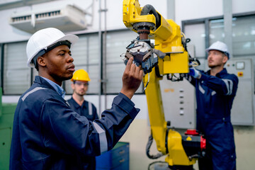 African American engineer or technician worker hold part of robotic arm and check  the function of machine and co-worker support in the back in factory workplace.