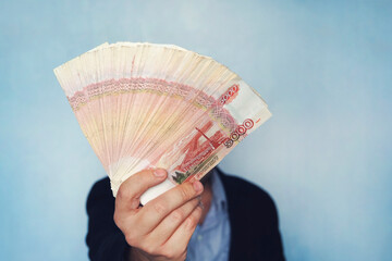 lot of money in the hand of a young businessman on a blue background. A stack of banknotes of Russian rubles with a face value of 5000 rubles. successful businessman