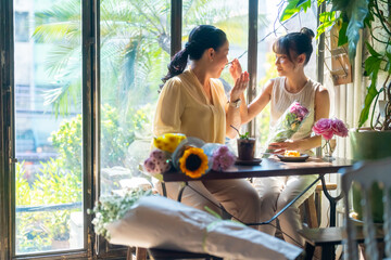 Happy Asian mother and daughter sitting by the window in coffee shop with drinking coffee and eating cake together. Happy family enjoy outdoor lifestyle shopping in the city on summer holiday vacation