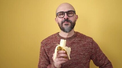 Sticker - Young bald man smiling confident eating banana over isolated yellow background