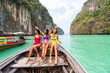 Group of Asian woman friends in swimwear sitting on ship bow and looking beautiful island beach during travel on boat in summer sunny day. Attractive girl enjoy outdoor lifestyle on holiday vacation.