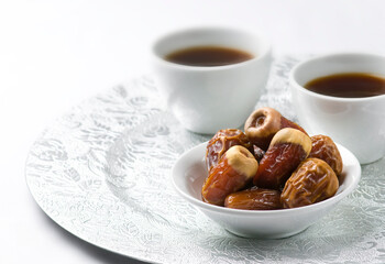 A bowl of dates and two cups of black coffee in silver plate. Popular Middle Eastern beverage- black coffee and sweet dates served in a modern tea cups.