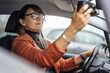 © olezzo - Adult caucasian businesswoman in glasses adjusting the rearview mirror while sitting at the wheel of a car