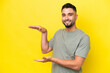 © luismolinero - Young Arab handsome man isolated on yellow background holding copyspace to insert an ad