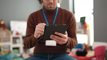 Poster - Young hispanic man preschool teacher writing on touchpad standing at kindergarten