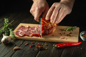 The hands of the cook with a knife cut into small pieces the baked beef on the kitchen cutting board. The concept of fast food or making sandwiches on a black background