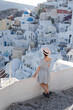 © biotin - Tourist woman in blue dress with hat relaxing at sea view in the traditional village Oia. Walking Santorini tour, Greece, during her summer  crouise travel. European tourism attraction in Greece.