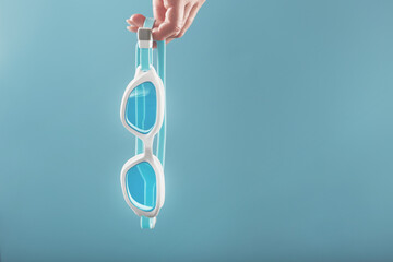 White swimming glasses in hand with a blue lens on a blue background