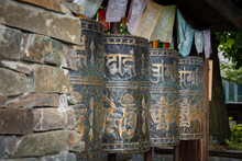 A Row Of Metal Tibetan Buddhist Prayer Wheels With Golden Matra Letters. 