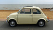 Classic Cream Coloured Fiat 500 parked on seafront promenade beach and sea in background.