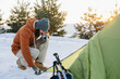 Tourist in snowy mountains. A young man sets up a tent for the night in a snowy forest at sunset.