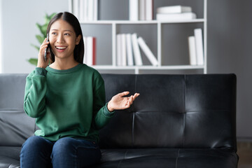 Poster - Pretty Asian girl having a phone call with her friends while sitting on the sofa in her living room.