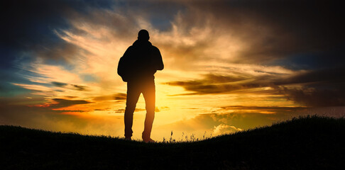 man with backpack walks alone on the hill at sunset.