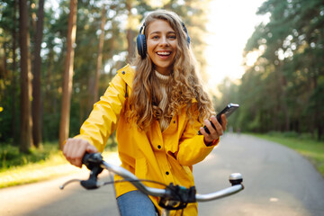 Pretty young womanusing mobile phone in the city while listening music through earphones to go by the bicycle in the park. Lifestyle. Relax, nature concept.