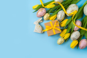 Wall Mural - Easter holiday background with easter eggs, gift box and yellow  tulip flowers. Top view, flat lay