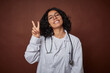 © Asier - Young colombian doctor woman with stethoscope joyful and carefree showing a peace symbol with fingers.