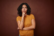 Young colombian curly hair woman isolated on brown background looking sideways with doubtful and skeptical expression.