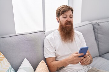 Wall Mural - Young redhead man using smartphone with serious expression at home