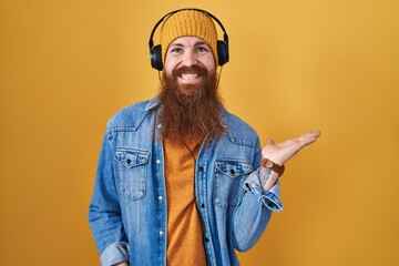 Canvas Print - Caucasian man with long beard listening to music using headphones smiling cheerful presenting and pointing with palm of hand looking at the camera.