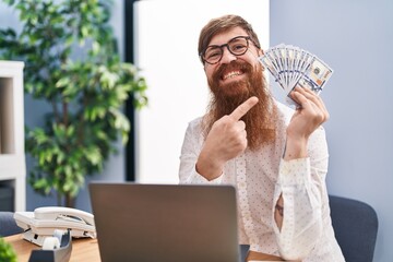 Canvas Print - Caucasian man with long beard working using computer laptop holding dollars smiling happy pointing with hand and finger