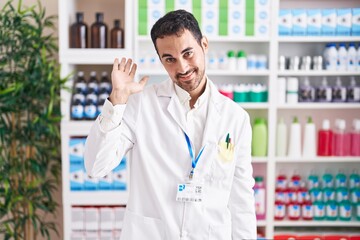 Poster - Handsome hispanic man working at pharmacy drugstore waiving saying hello happy and smiling, friendly welcome gesture