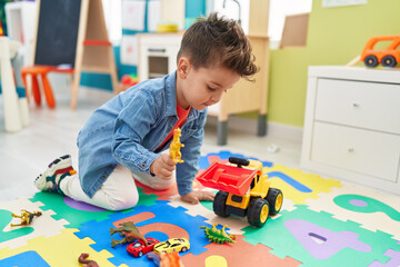 Sticker - Adorable hispanic toddler playing with tractor and dino toy sitting on floor at kindergarten