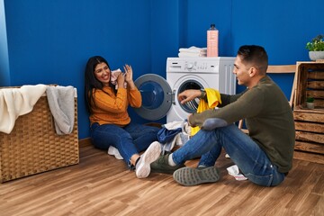 Wall Mural - Man and woman couple smiling confident playing with clothes at laundry room