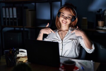 Wall Mural - Young caucasian woman working at the office at night looking confident with smile on face, pointing oneself with fingers proud and happy.