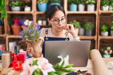 Wall Mural - Young hispanic woman working at florist shop doing video call mouth and lips shut as zip with fingers. secret and silent, taboo talking