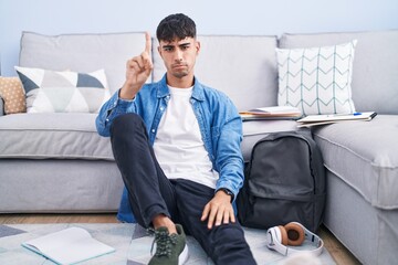 Sticker - Young hispanic man sitting on the floor studying for university pointing with finger up and angry expression, showing no gesture