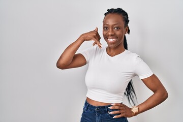 Wall Mural - Beautiful black woman standing over isolated background smiling doing phone gesture with hand and fingers like talking on the telephone. communicating concepts.