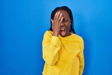 Wall Mural - Beautiful black woman standing over blue background yawning tired covering half face, eye and mouth with hand. face hurts in pain.