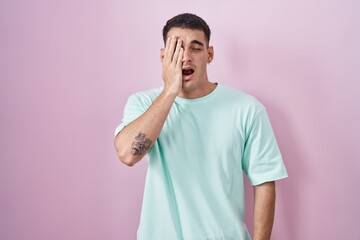 Wall Mural - Handsome hispanic man standing over pink background yawning tired covering half face, eye and mouth with hand. face hurts in pain.