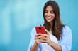 © CarlosBarquero - A young girl using a cell phone with a blue background. A smiling woman flirting through an app. Dating website in the new era of human relationships through the internet.