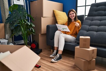 Sticker - Young brunette woman sitting on the sofa at new home looking at documents pointing finger to one self smiling happy and proud