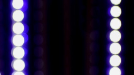 Wall Mural - Vertically falling blur light circles. White bokeh with a blue outline and reflexes fall down on a black background. Linear motion of glowing bokeh in rows.