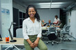© CarlosBarquero - Portrait of smiling young African American professional female sitting at modern office desk. Happy mixed race business woman team leader posing for photo at corporate meeting. Concept of workplace.