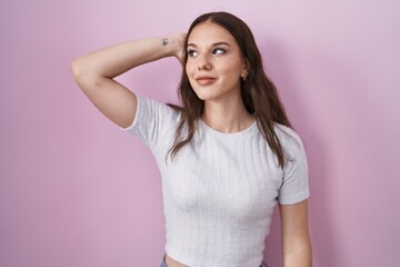 Poster - Young hispanic girl standing over pink background smiling confident touching hair with hand up gesture, posing attractive and fashionable