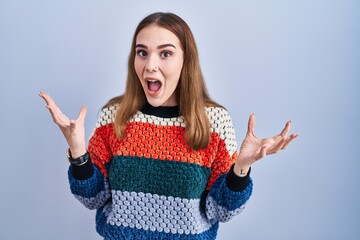 Poster - Young hispanic girl standing over blue background celebrating crazy and amazed for success with arms raised and open eyes screaming excited. winner concept