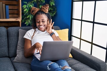 Poster - African woman with braided hair using laptop at home smiling with hand over ear listening and hearing to rumor or gossip. deafness concept.