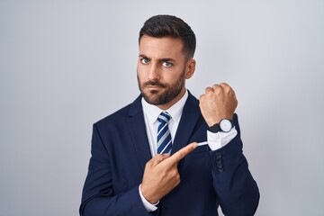 Poster - Handsome hispanic man wearing suit and tie in hurry pointing to watch time, impatience, looking at the camera with relaxed expression