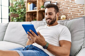 Canvas Print - Young hispanic man smiling confident using touchpad at home