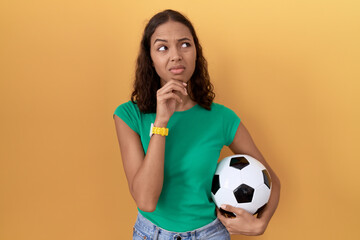 Wall Mural - Young hispanic woman holding ball thinking worried about a question, concerned and nervous with hand on chin